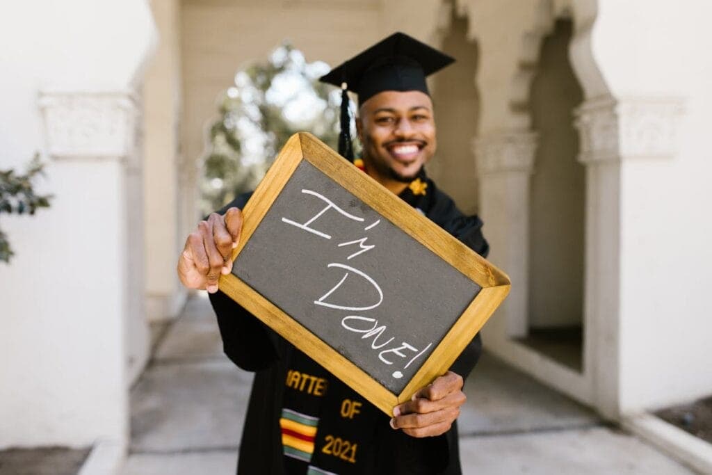 man wearing graduation regalia holding a chalkboard